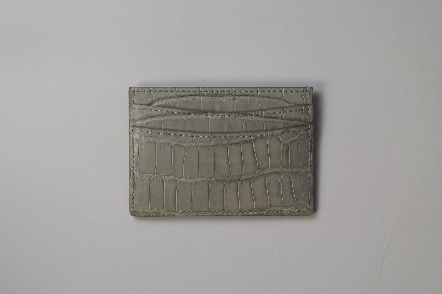 a grey crocodile card holder on a white surface