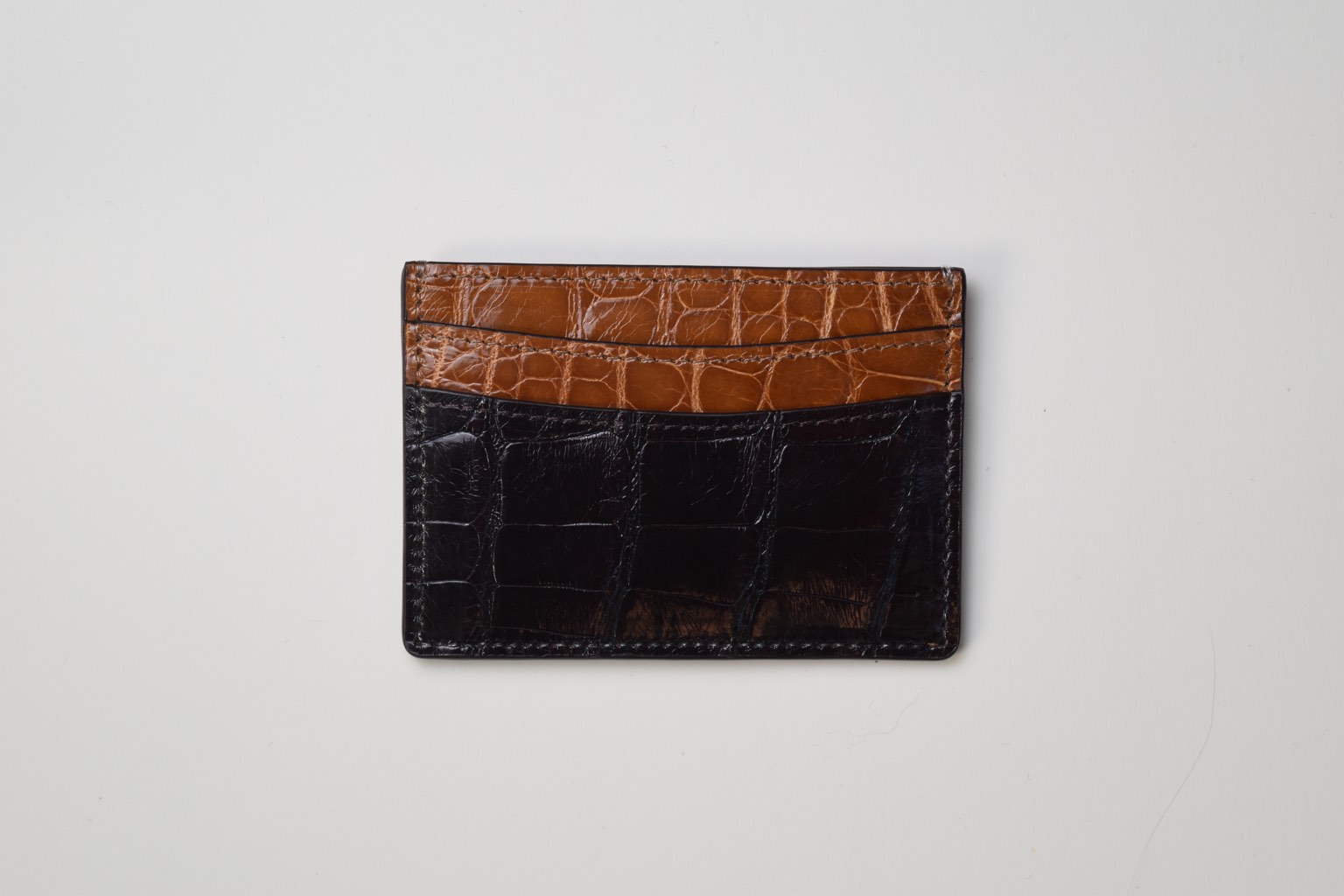 a black and tan crocodile wallet on a white surface